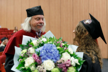 A graduate in a toga presents flowers to a man (former dean) in a toga.