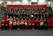 Lecture hall. In the front rows sit teachers in academic togas. In the back stand graduates in student togas.