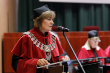 Graduation ceremony. A woman (dean) in an academic robe speaks into the microphone.