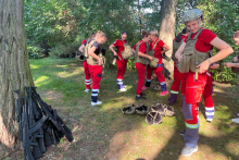 Several women are standing in the clearing. They are wearing red lifeguard outfits. They wear bulletproof vests. Some have helmets. 