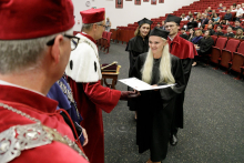 A man in a red toga congratulates a woman in a black toga.