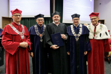 Five men in togas, three in black, two in red. They pose for a photo.