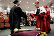 A man in a red toga congratulates a man in a black toga.