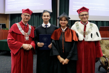 Four people in togas pose for a photo. Two men in red, one in black and one woman in black.