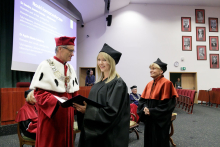 A man in a red toga congratulates a woman in a black toga.