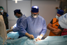 A doctor in surgical garb performs the procedure.