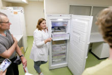 Kobieta w białym fartuchu stoi przy otwartej lodówce. 