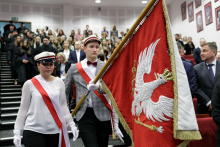 Dwie młode osoby ubrane na galowo niosące sztandar z godłem WUM - orłem na czerwonym tle