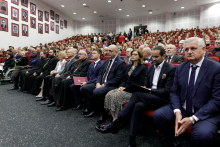 A collection of people of different ages, dressed elegantly, sit on red chairs.