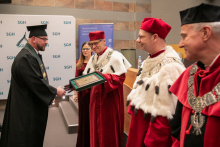 A group of people dressed in academic togs. They present a diploma.