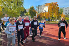 Biegnąca grupa osób ubranych w stroje sportowe. Biegną po boisku szkolnym.