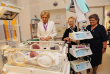 Trzy kobiety stojące nad inkubatorem, w inkubatorze leży niemowlę.