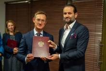 Two men in suits. Together they hold a diploma