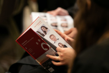 Human hands holding a book, flicking through the pages, photos of graduates can be seen on the pages.