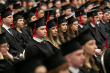 A group of young people, men and women, dressed in black academic togas, look in one direction.