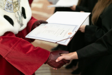 Two people holding a diploma, one in a red and white toga, the other in black.