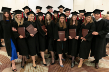 A group of young people dressed in black academic outfits pose for a photo with their diplomas in brown covers.