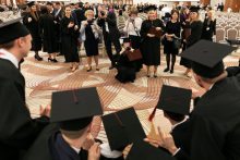 A group of young people dressed in academic togs pose for a photo.