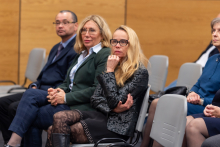 Three people sit in a row on chairs. Two women and one man.