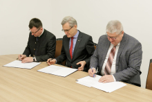 Three men sit at a table and sign documents