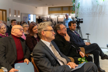 The audience in the lecture hall. Three men sit in the front row. 