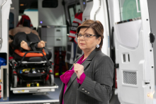 In the foreground a woman in a gray jacket, behind her an ambulance simulator