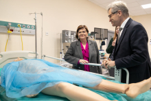 A man and a woman stand by a hospital bed on which a mannequin lies