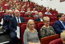 Grupa osób w różnym wieku, siedzą na czerwonych fotelach w auli wykładowej.