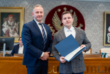 Dwóch mężczyzn, elegancko ubranych, pozuje do zdjęcia. Mężczyzna po prawej trzyma w rękach teczkę.