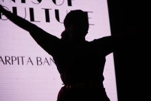 A silhouette of a person with arms spread out. The person is standing against a bright screen. On the screen is the text: “SPIRITS OF CULTURE”. The background is bright and the figure can be seen as a dark outline.