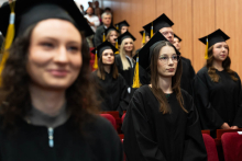 A group of young pharmacy graduates face the center of the auditorium. They are in the process of repeating the words of the oath. They are wearing black togas and birettas.