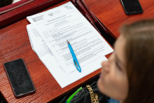 On a wooden desk lie two smartphones, a blue pen and a sheet of paper. The top sheet contains the heading “CONFERENCE PROGRAMME 2025”.