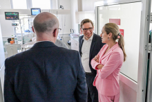 Three formally dressed individuals are talking in a hospital room with medical equipment.