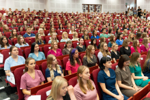 Graduation ceremony for nursing and midwifery graduates. A group of young women and men sitting in an auditorium, dressed in colorful medical uniforms: pink, blue, green, and purple.