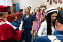 Graduation ceremony for nursing and midwifery graduates. Young women in medical uniforms and nursing caps stand in line before an older man in a red gown, who hands them their diplomas.