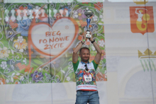 Na scenie mążczyzna w sportowej koszulce podnosi do góry puchar