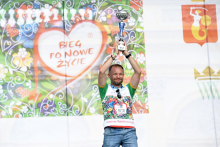 On stage, a man in a sports shirt raises a trophy.
