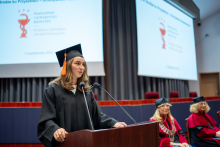 A person in a gown is speaking at a podium during the graduation ceremony.