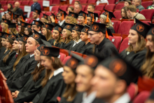 A group of graduates in gowns and mortarboards is seated in rows during the diploma awarding ceremony.