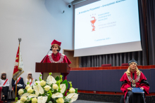 A person in academic attire is speaking at a podium during a graduation ceremony.