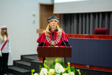 A person in academic attire is speaking at a podium during a graduation ceremony.