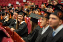 Graduates in gowns and caps with orange tassels are seated in rows during the graduation ceremony.