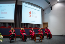 Five people in gowns are seated on stage during the graduation ceremony.