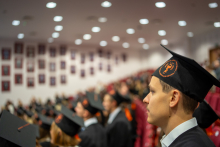 A group of graduates in gowns and caps is seated in an auditorium during the graduation ceremony.