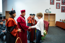 A student, the dean, the vice deans, and the vice president stand in the middle of the auditorium. The student and the vice president shake hands. Everyone is smiling.