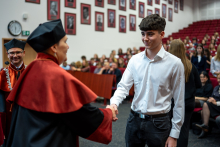 The vice dean shakes hands with a student wearing a blue shirt. Other people can be seen in the background.