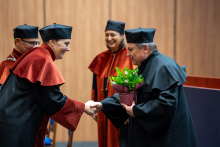 The dean and vice deans present flowers to Dr. Białek. Everyone is smiling.