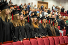 Grupa absolwentów w togach i biretach stoi w rzędzie podczas ceremonii dyplomatorium
