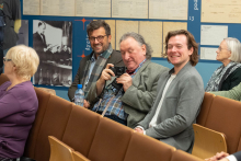 Pięć osób siedzi w audytorium. W pierwszym rzędzie znajdują się trzej mężczyźni, z których jeden trzyma aparat fotograficzny.