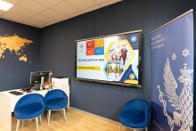A bright room. On the left, you can see a white desk with blue chairs, and on the right, a WUM rollup banner. On the wall, there is a screen displaying information about the Welcome Center.